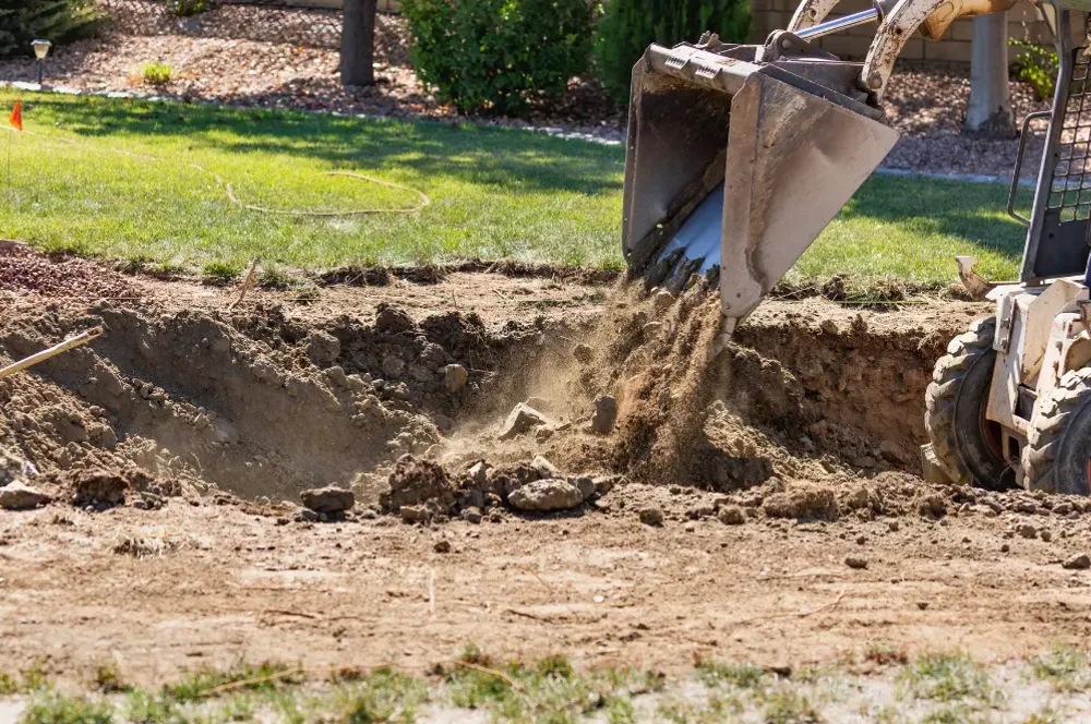 An excavator shaping soil alongside a residential lawn